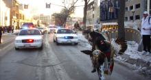 Photo: Native American dressed in traditional garb in front of a flashing cop cars