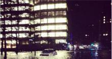 Photo of Goldman Sachs building completely lit while a car floats on the flooded streets