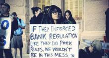 Woman holding sign reading, "If they enforced bank regulation like they do park rules, we wouldn't be in this mess in the first place."