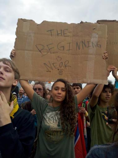 Photo of woman holding a sign reading, "The Beginning is Near"