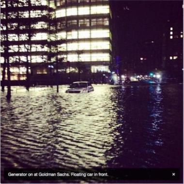 Photo of Goldman Sachs building completely lit while a car floats on the flooded streets